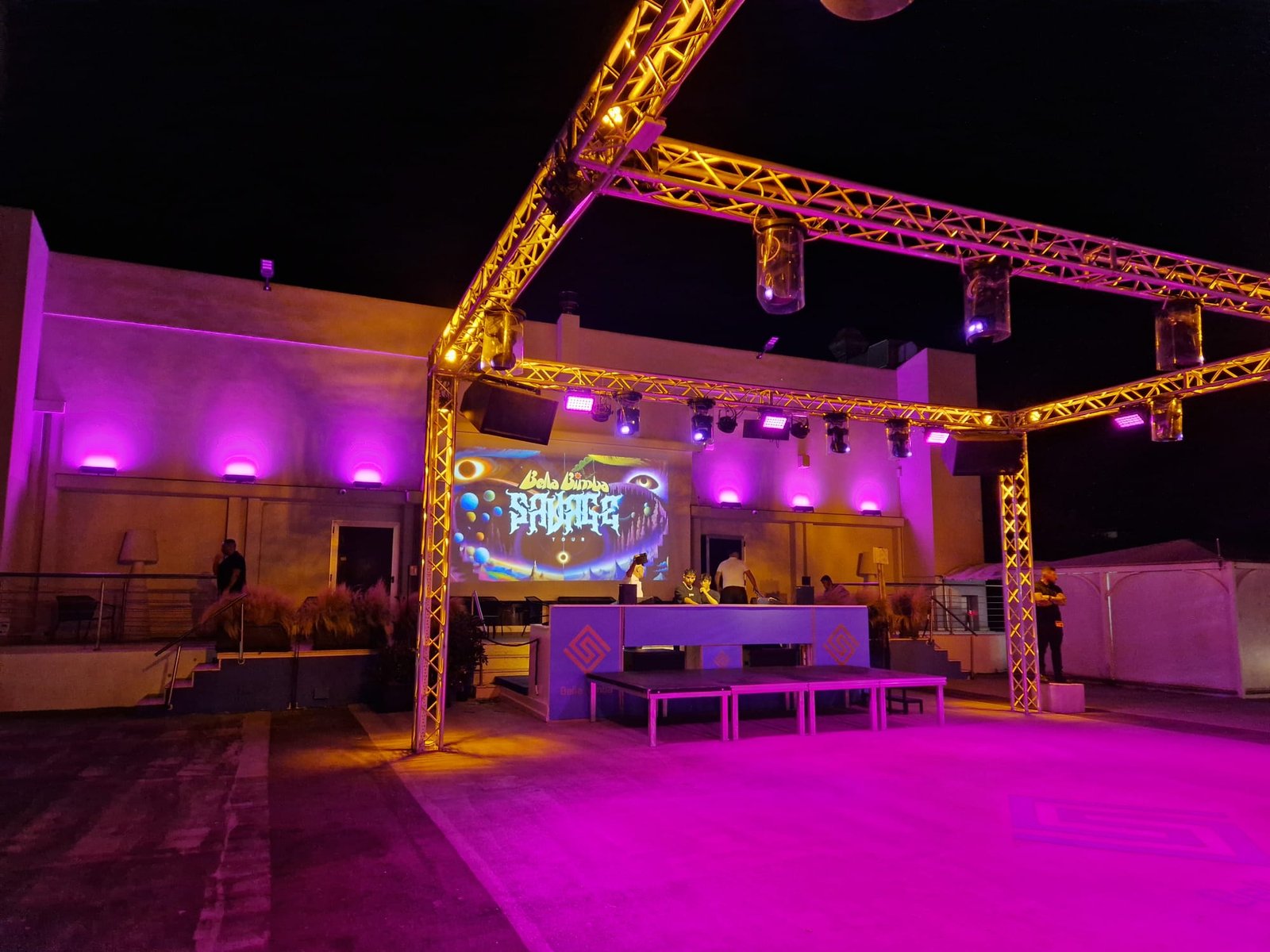Struttura luci con illuminazione viola e videoproiezione sopra la postazione DJ