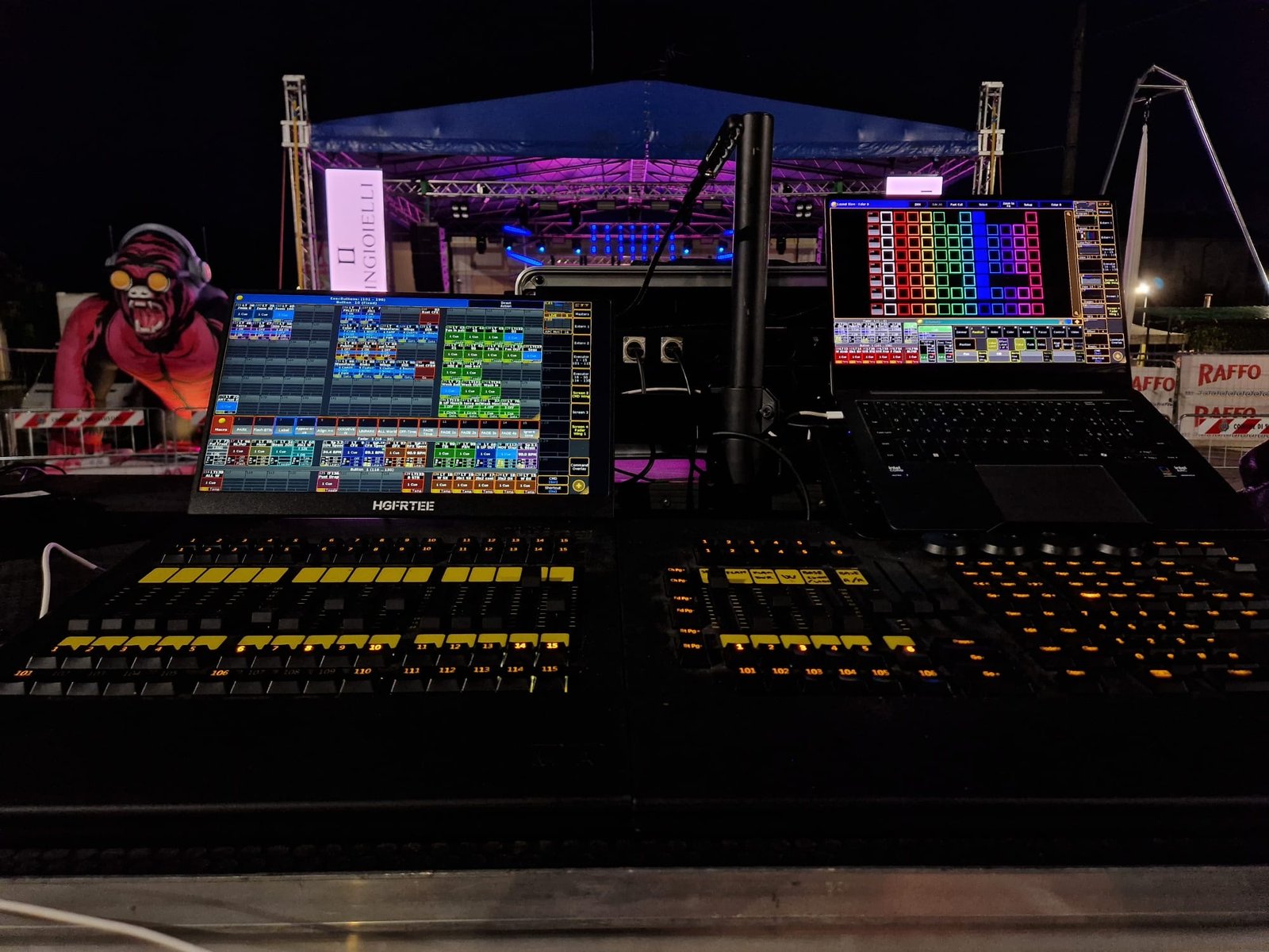 Schermi e console di regia davanti a un palco all’aperto di sera