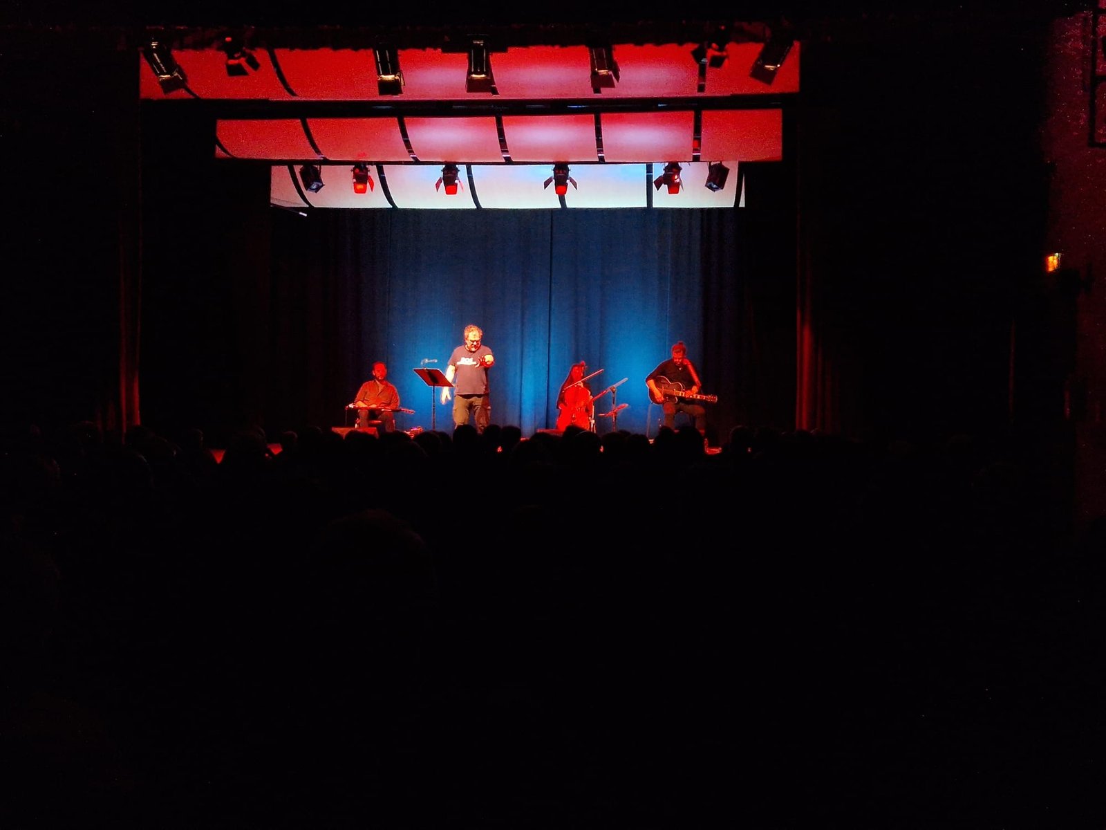 Artisti e musicisti sul palco di un teatro illuminato in rosso e blu